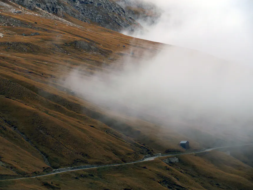 Nebel zieht über den herbstlichen Hang, darunter eine Hütte