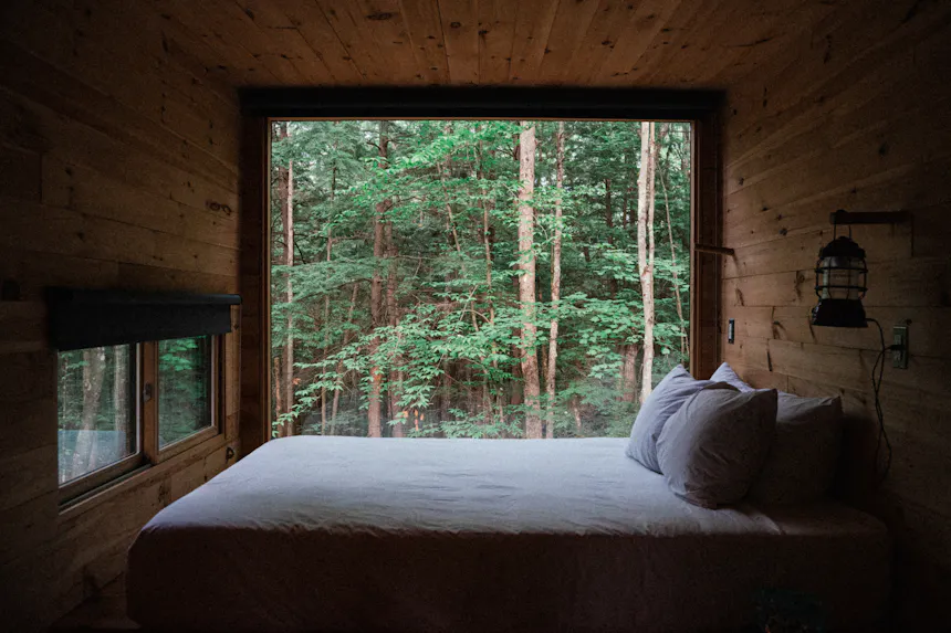 Bett vor einem raumhohen Fenster mit Blick in den Wald